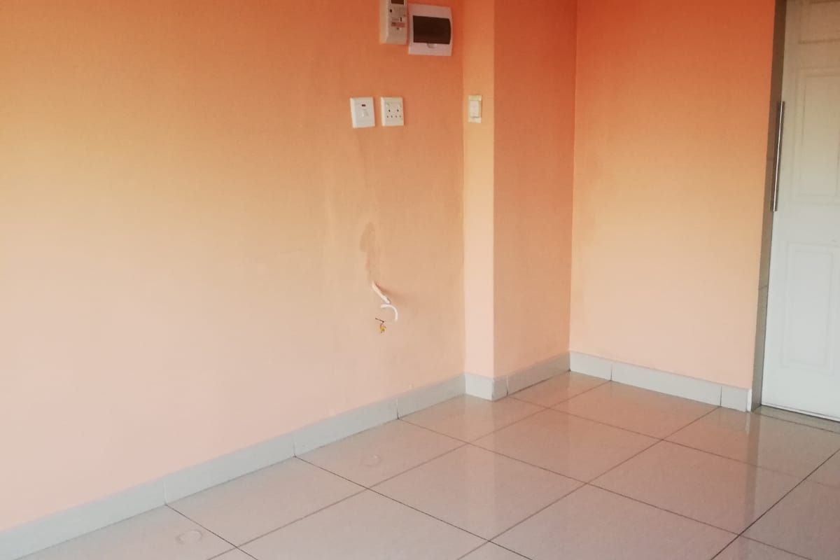 An empty living area featuring tiled flooring, peach-toned walls, and visible electrical infrastructure. The space is ready for renovation or staging.