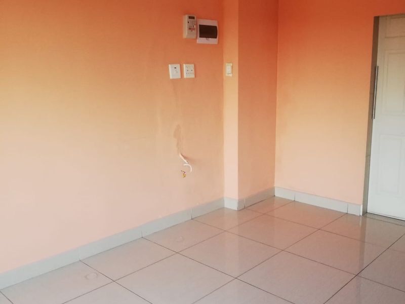An empty living area featuring tiled flooring, peach-toned walls, and visible electrical infrastructure. The space is ready for renovation or staging.