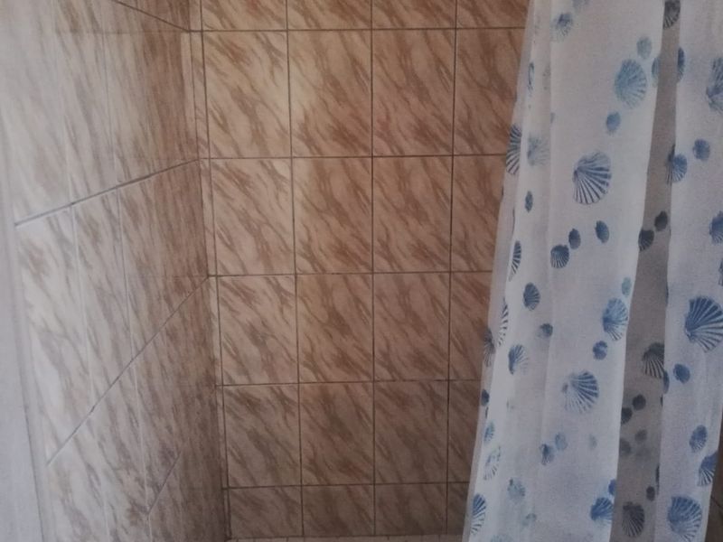 A shower enclosure featuring dated brown patterned wall tiles and a tiled floor base.