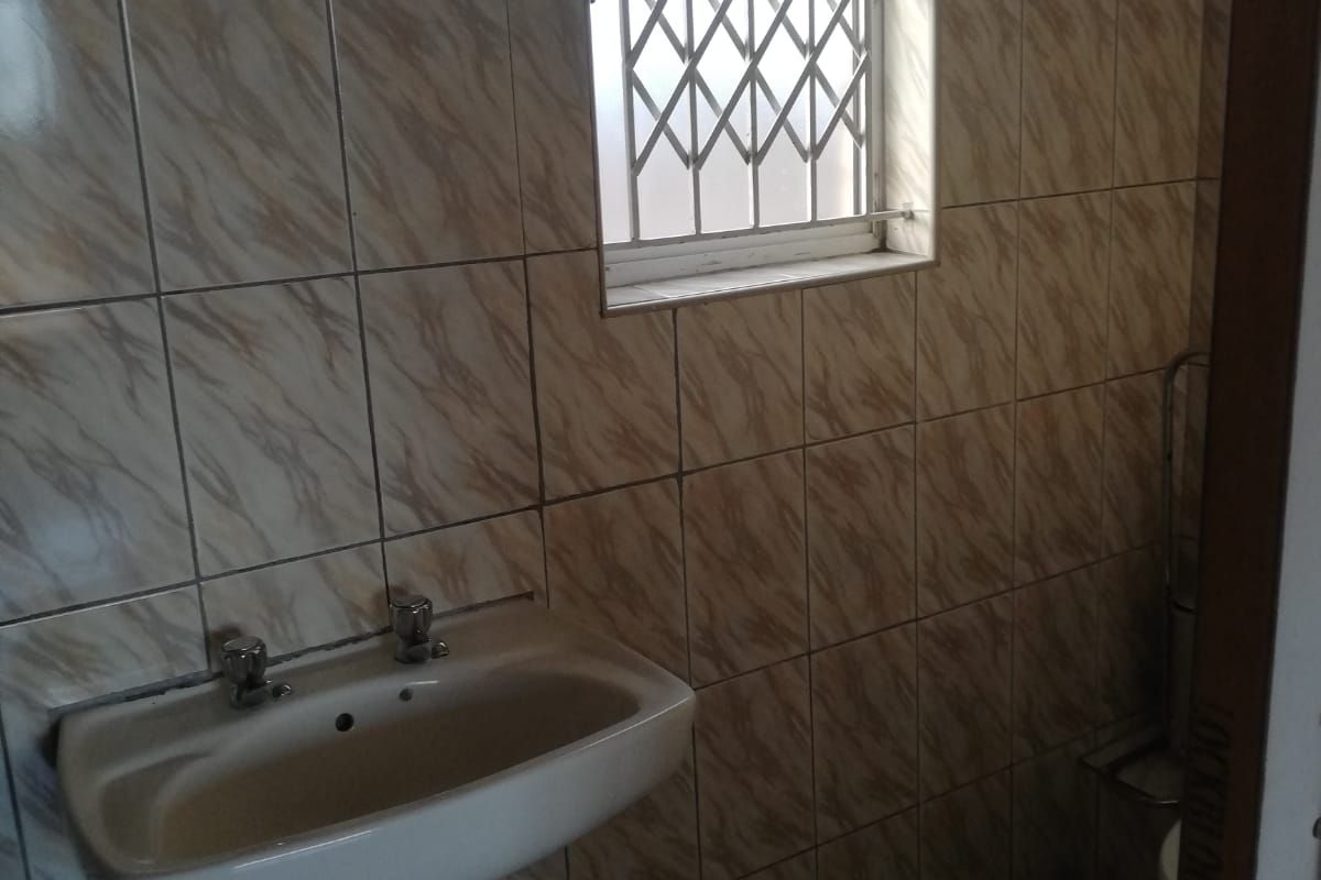 A functional bathroom featuring a pedestal basin, fully tiled walls, and a window fitted with a security gate.