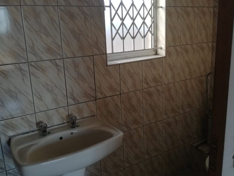 A functional bathroom featuring a pedestal basin, fully tiled walls, and a window fitted with a security gate.