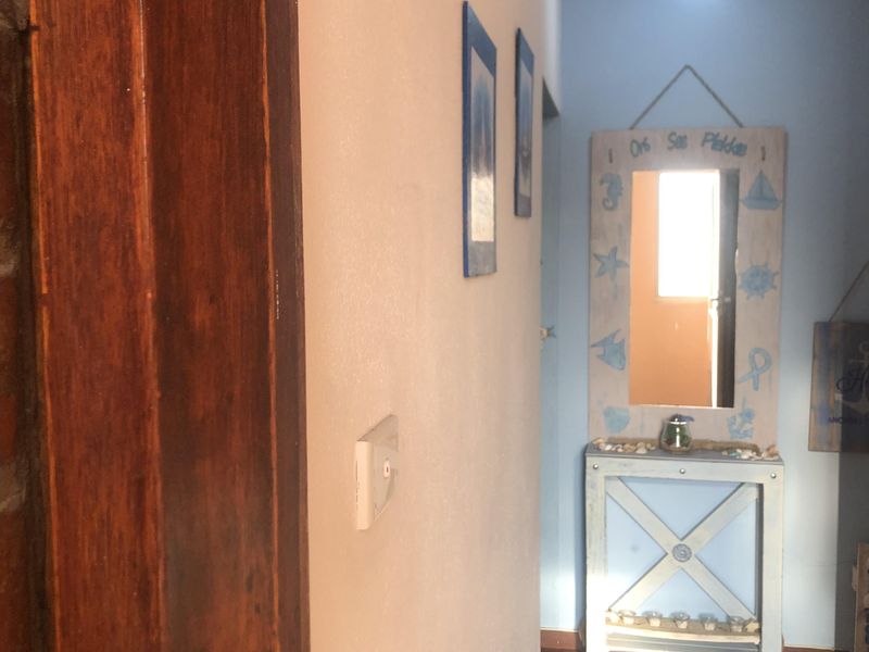 A narrow hallway featuring dark parquet flooring and a wooden door frame, leading towards a light-filled area at the end.