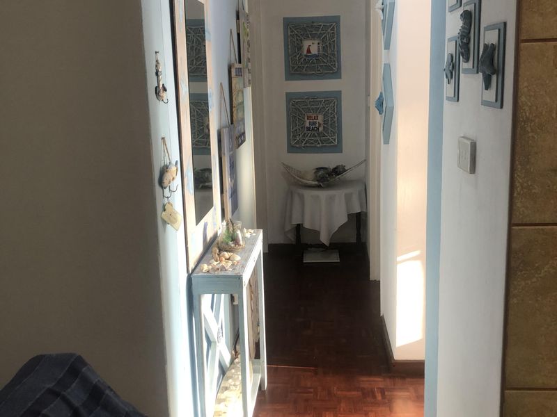 A narrow hallway featuring warm-toned parquet flooring and neutral wall finishes, providing a transition between living spaces.