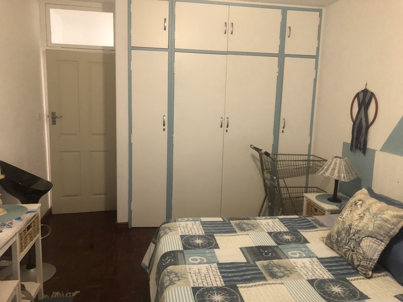 A bedroom featuring built-in cupboards with overhead storage, parquet flooring, and a transom window above the door.