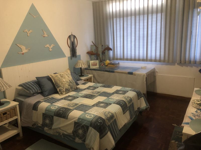 A bedroom featuring parquet flooring and vertical blinds, offering a functional space with neutral wall finishes.