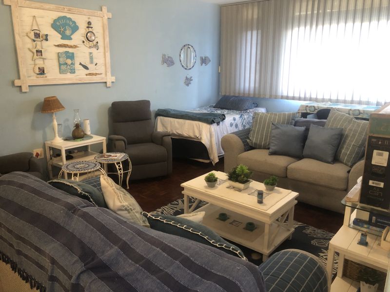 A living room featuring parquet flooring and vertical blinds, currently furnished with a multi-purpose seating and sleeping arrangement.