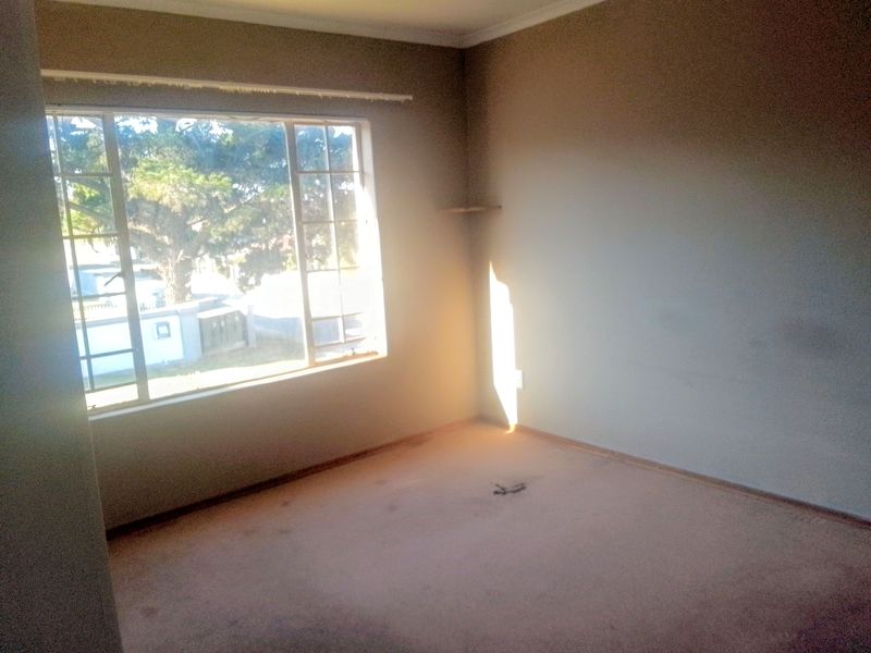 An empty bedroom featuring a large window, carpeted flooring, and neutral wall finishes, offering a blank canvas for potential renovation or staging.