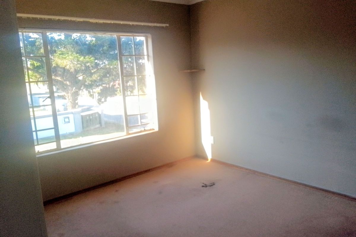 An empty bedroom featuring a large window, carpeted flooring, and neutral wall finishes, offering a blank canvas for potential renovation or staging.