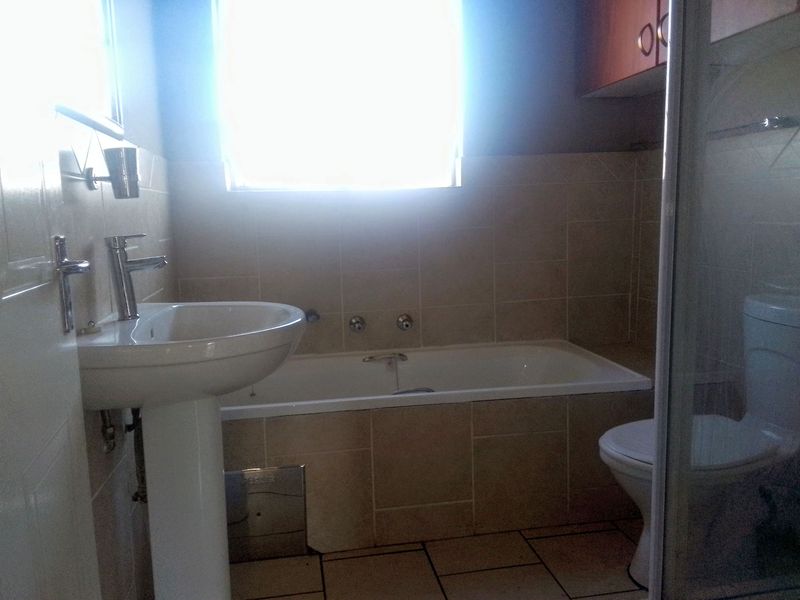 A functional bathroom featuring a pedestal basin, built-in bathtub, toilet, and a separate shower enclosure with neutral wall and floor tiling.