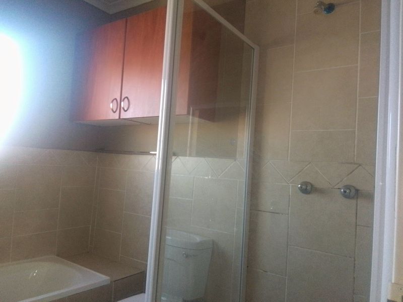 A functional bathroom featuring a shower enclosure, tiled walls, and built-in cabinetry, providing essential utility in a compact layout.