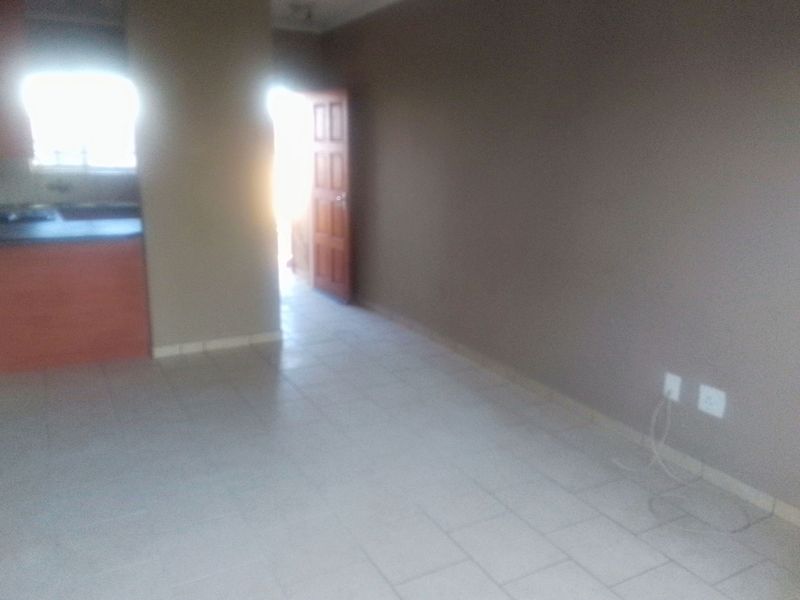 An empty open-plan living and kitchen area featuring tiled flooring and neutral wall tones, providing a blank canvas for interior design.