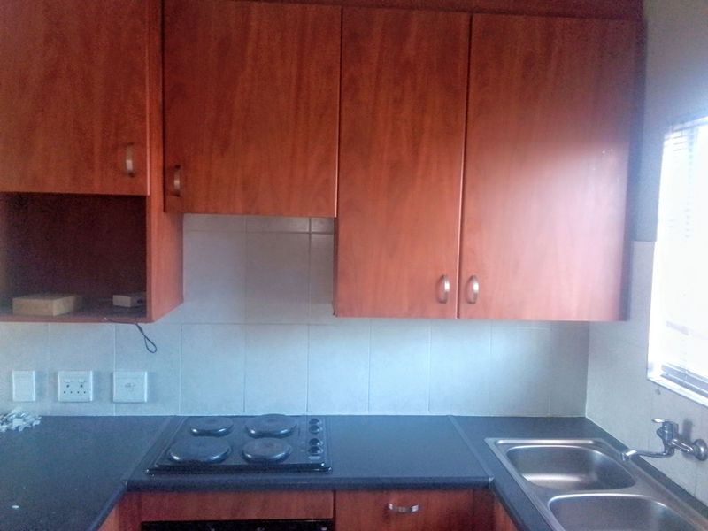 A functional kitchen area featuring wood-look laminate cabinetry, a built-in electric hob, double bowl sink, and tiled splashback.
