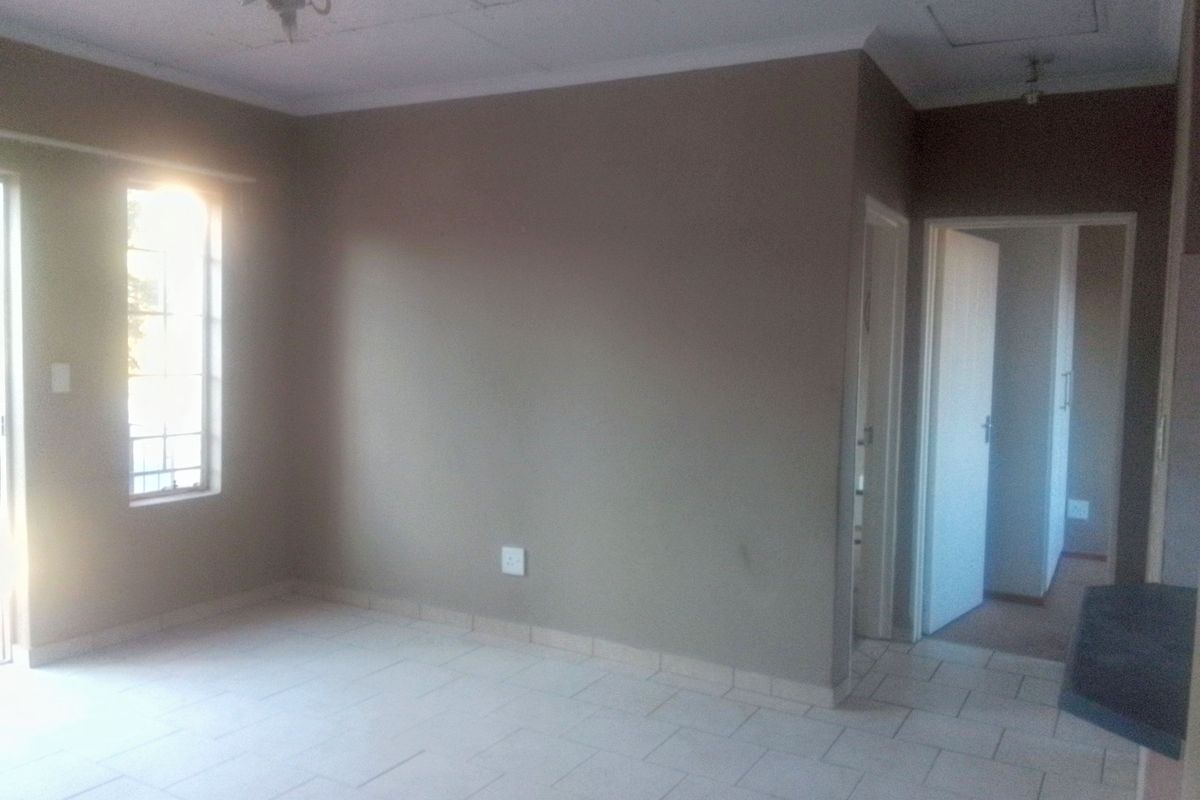 An empty living room featuring tiled flooring, neutral wall paint, and natural light from a window with security bars.