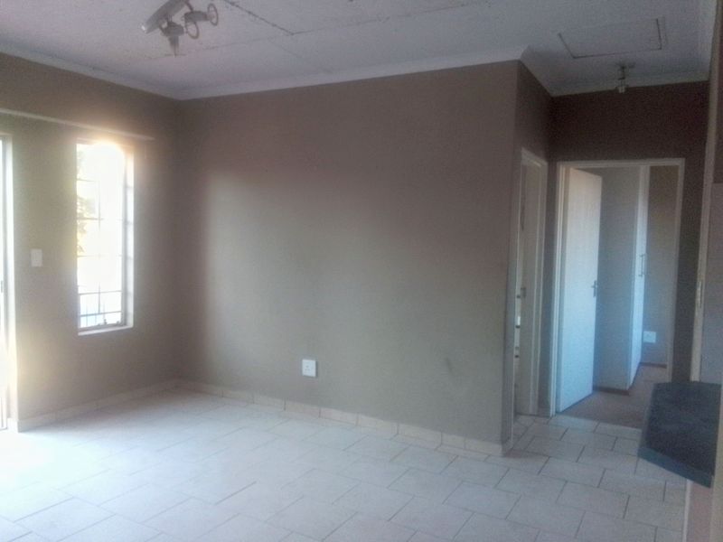 An empty living room featuring tiled flooring, neutral wall paint, and natural light from a window with security bars.