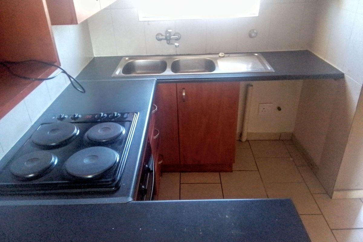 A compact kitchen featuring built-in wooden cabinetry, dark laminate countertops, a double bowl sink, and an integrated electric hob with tiled splashbacks.