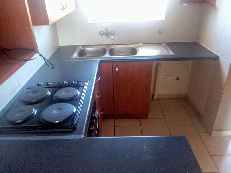 A compact kitchen featuring built-in wooden cabinetry, dark laminate countertops, a double bowl sink, and an integrated electric hob with tiled splashbacks.