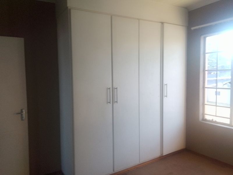 A bedroom featuring built-in cupboards and a window with security bars, offering a clean and functional space.