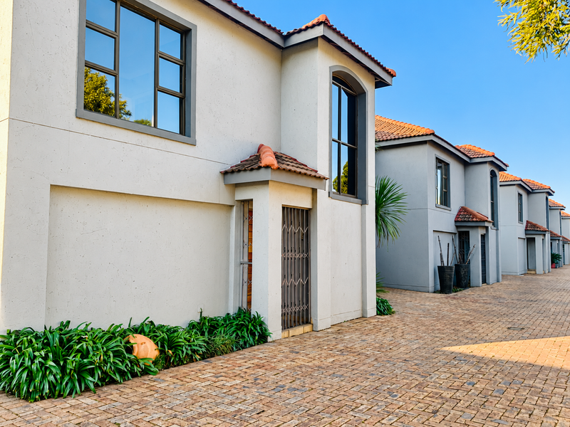 A well-maintained townhouse complex featuring modern grey facades, terracotta roof tiles, paved driveways, and secure entrance gates.