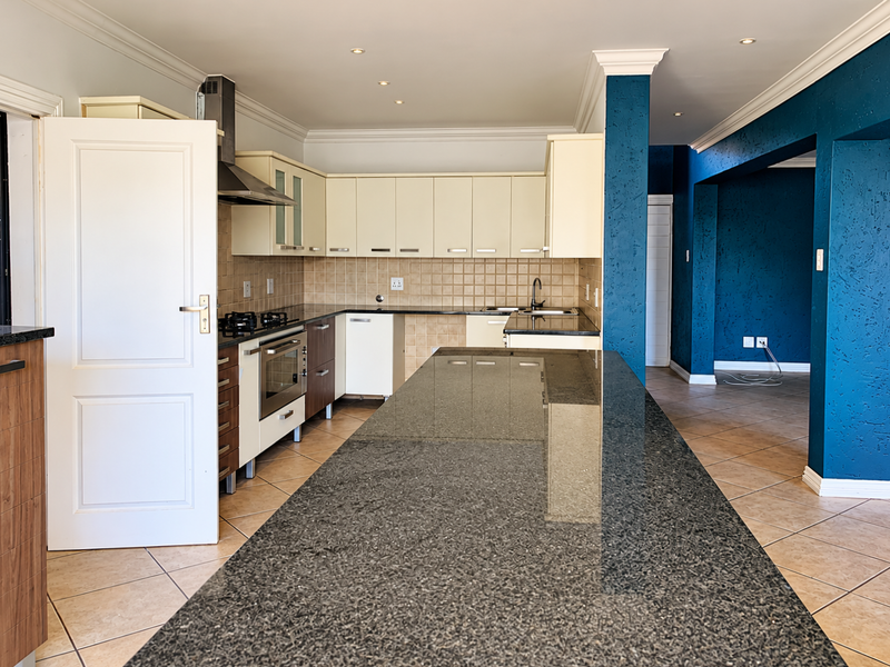 Spacious open-plan kitchen featuring a large granite island, built-in oven, gas hob, and ample cabinetry, seamlessly flowing into the adjacent living area.