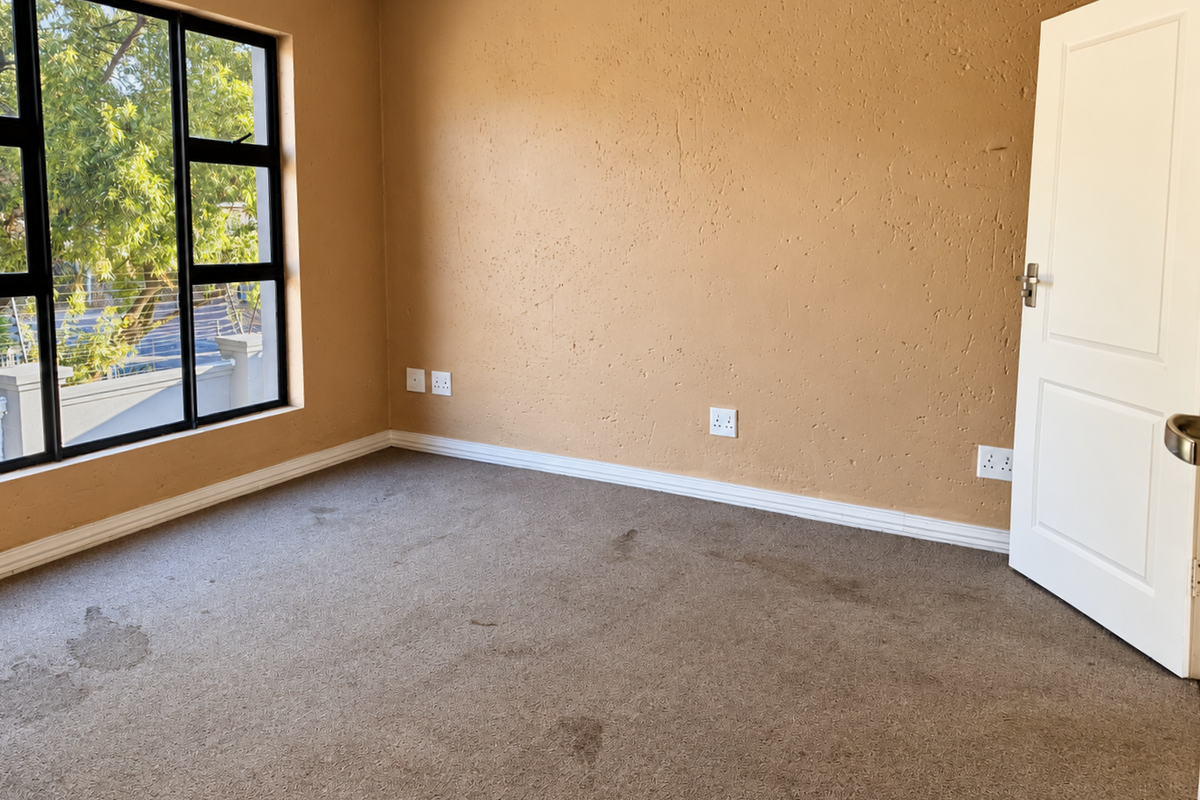 An empty bedroom featuring textured walls, aluminium-framed windows, and carpeted flooring in need of attention.
