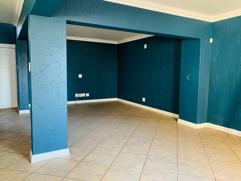 An empty, open-plan living area featuring teal-painted walls, tiled flooring, and crown molding, providing a blank canvas for interior design.