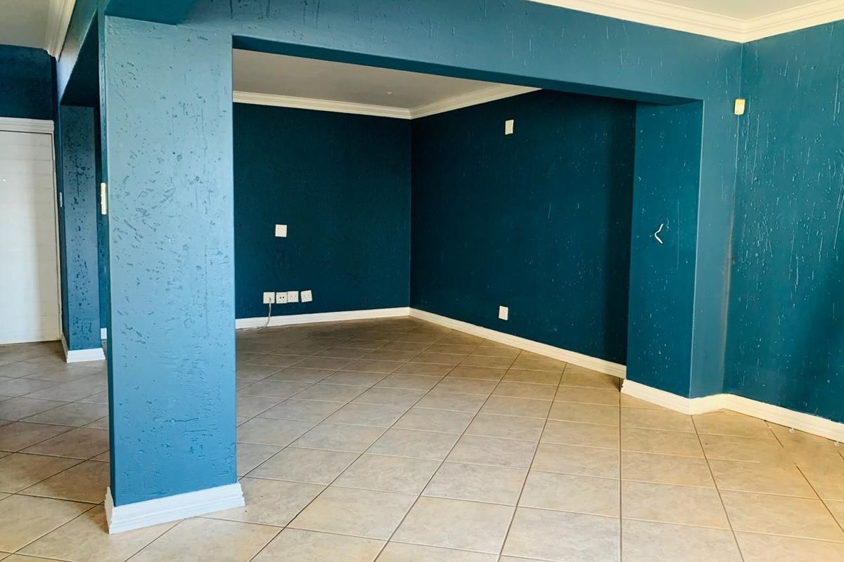 An empty, open-plan living area featuring teal-painted walls, tiled flooring, and crown molding, providing a blank canvas for interior design.