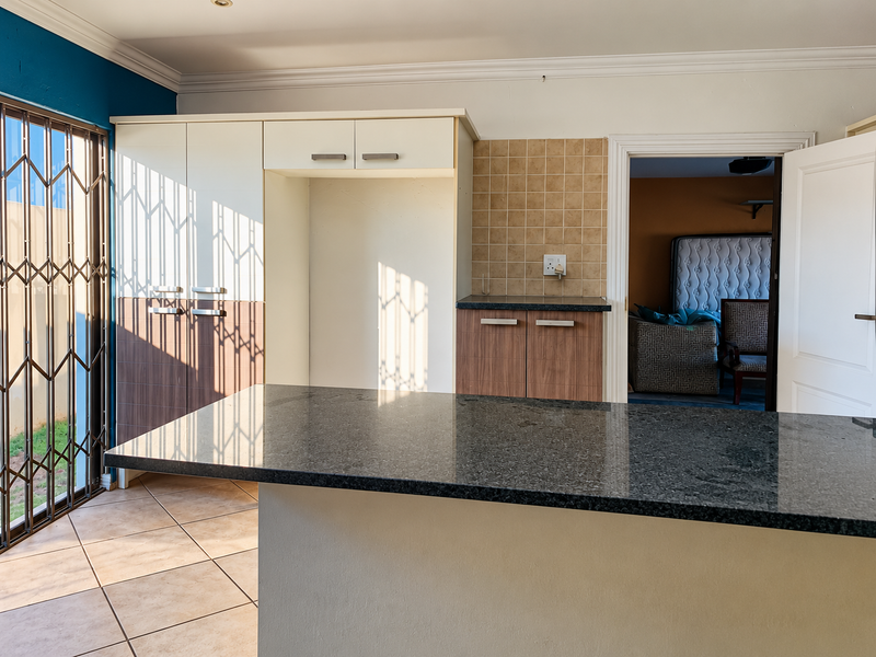 Kitchen area featuring a granite breakfast bar, built-in cabinetry, tiled backsplash, and direct access to the exterior through a security gate.