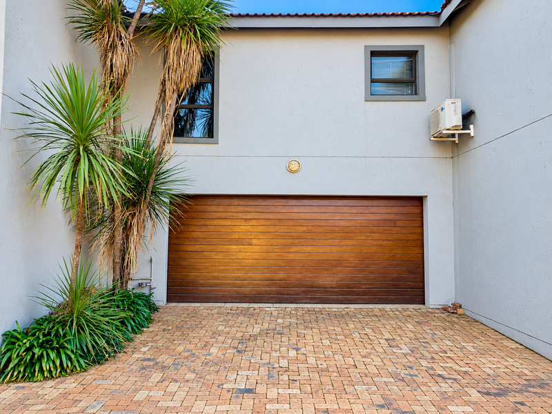 A well-maintained townhouse exterior featuring a modern wooden sectional garage door, paved driveway, and established landscaping.