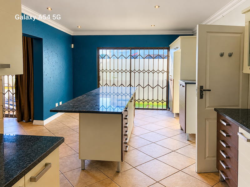 Spacious kitchen featuring a central island with granite countertops, ample cabinetry, tiled flooring, and direct access to the exterior through a security gate.