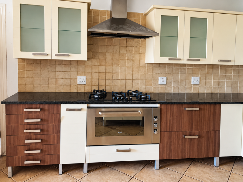A functional kitchen featuring two-tone cabinetry, granite countertops, a built-in gas hob, and a stainless steel extractor fan with a tiled backsplash.