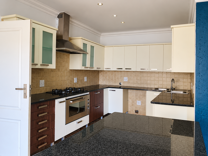 Modern kitchen featuring two-tone cabinetry, granite countertops, gas hob, built-in oven, stainless steel extractor fan, and a functional breakfast bar island.
