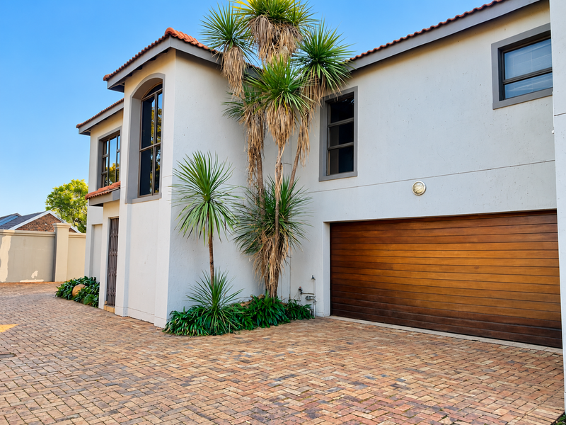 Front elevation of a modern townhouse featuring a double garage with timber door, paved driveway, and well-maintained exterior finishes.