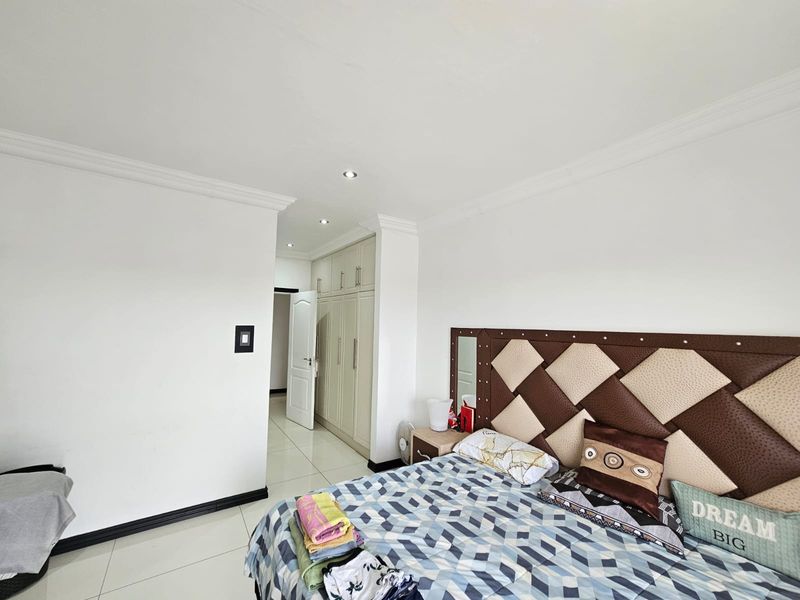 A well-maintained bedroom featuring neutral tiled flooring, built-in cupboards, and recessed downlighting.