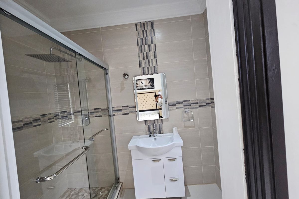Modern bathroom featuring a glass-enclosed shower with a rain shower head, a white vanity cabinet with a basin, and neutral wall tiling with mosaic accents.
