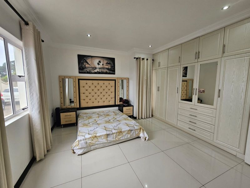 Spacious bedroom featuring large format floor tiles, extensive built-in cabinetry with integrated mirrors, and recessed ceiling lighting.