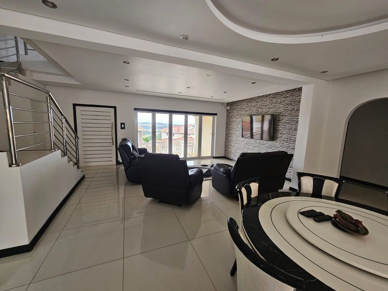 Spacious open-plan living and dining area featuring polished tile floors, a modern feature stone wall, and direct access to an outdoor balcony.