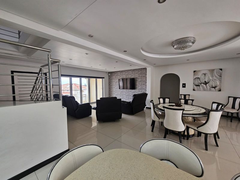 Spacious open-plan living and dining area featuring tiled floors, a feature stone wall, recessed ceiling lighting, and a modern staircase with stainless steel railings.