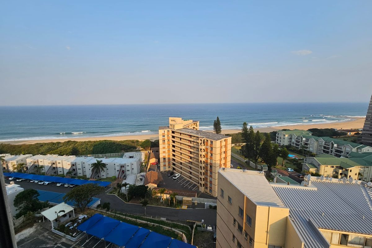 An elevated coastal view overlooking the ocean, surrounding residential apartment complexes, and parking areas.