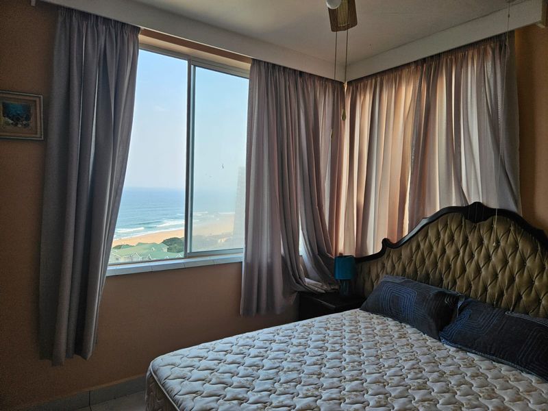 A bedroom featuring a large sliding window with ocean views and a ceiling fan.