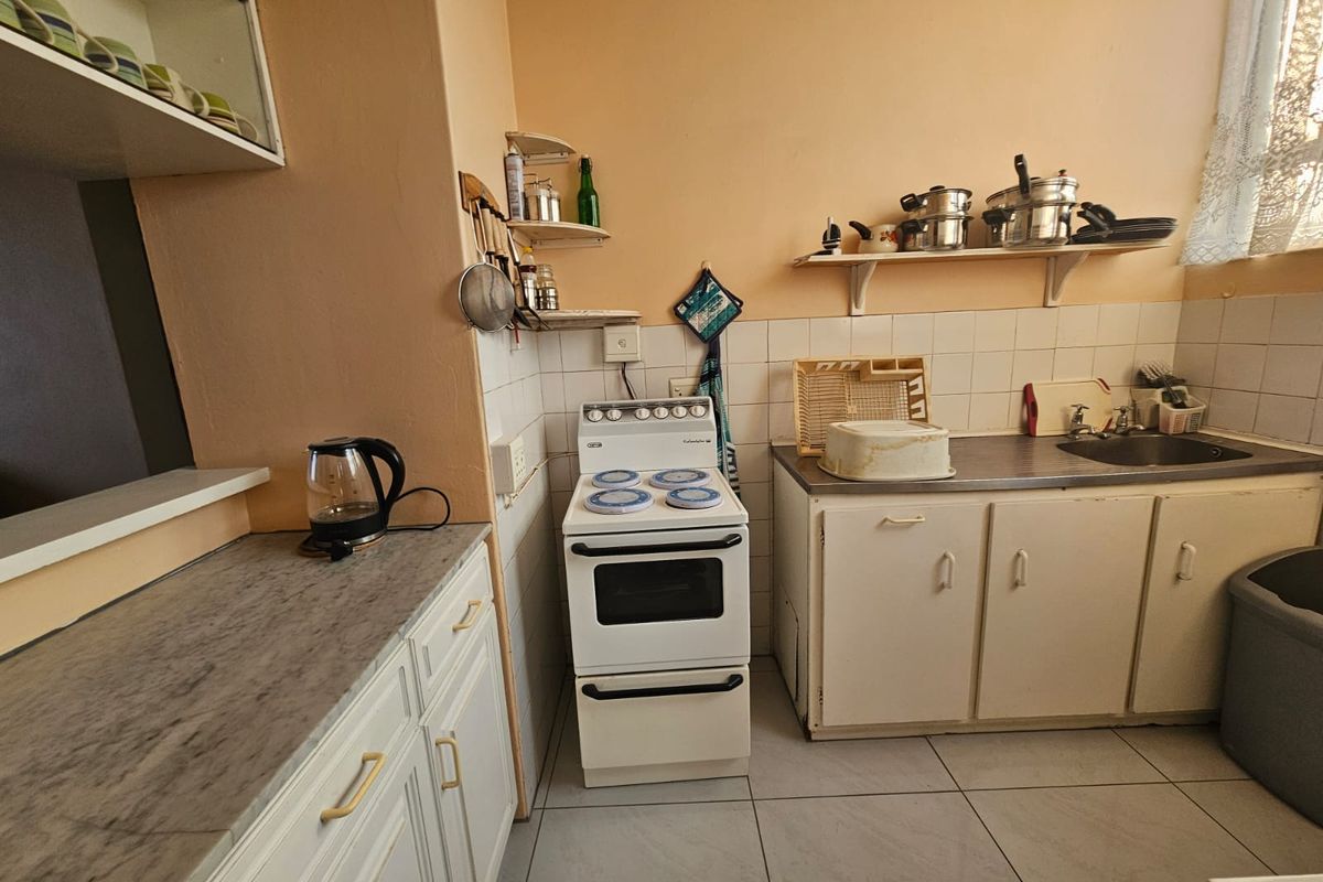 A functional kitchen featuring built-in cabinetry, a freestanding stove, tiled backsplash, and a stainless steel sink with ample counter space.