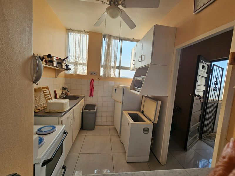 A functional kitchen featuring built-in cabinetry, tiled backsplash, and tiled flooring, offering a practical layout with potential for modern updates.