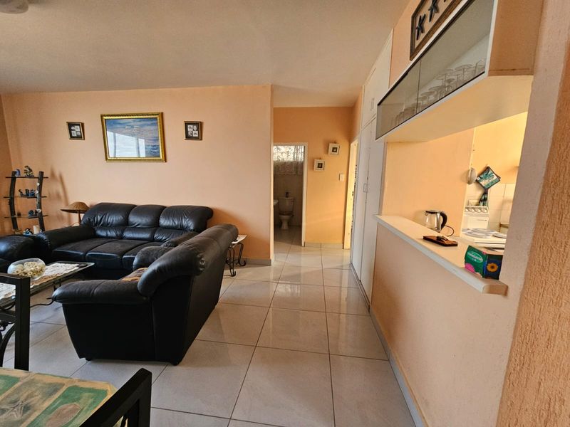 Open plan living area featuring tiled flooring, a breakfast counter, and built-in kitchen cabinetry with a glass-fronted display unit.