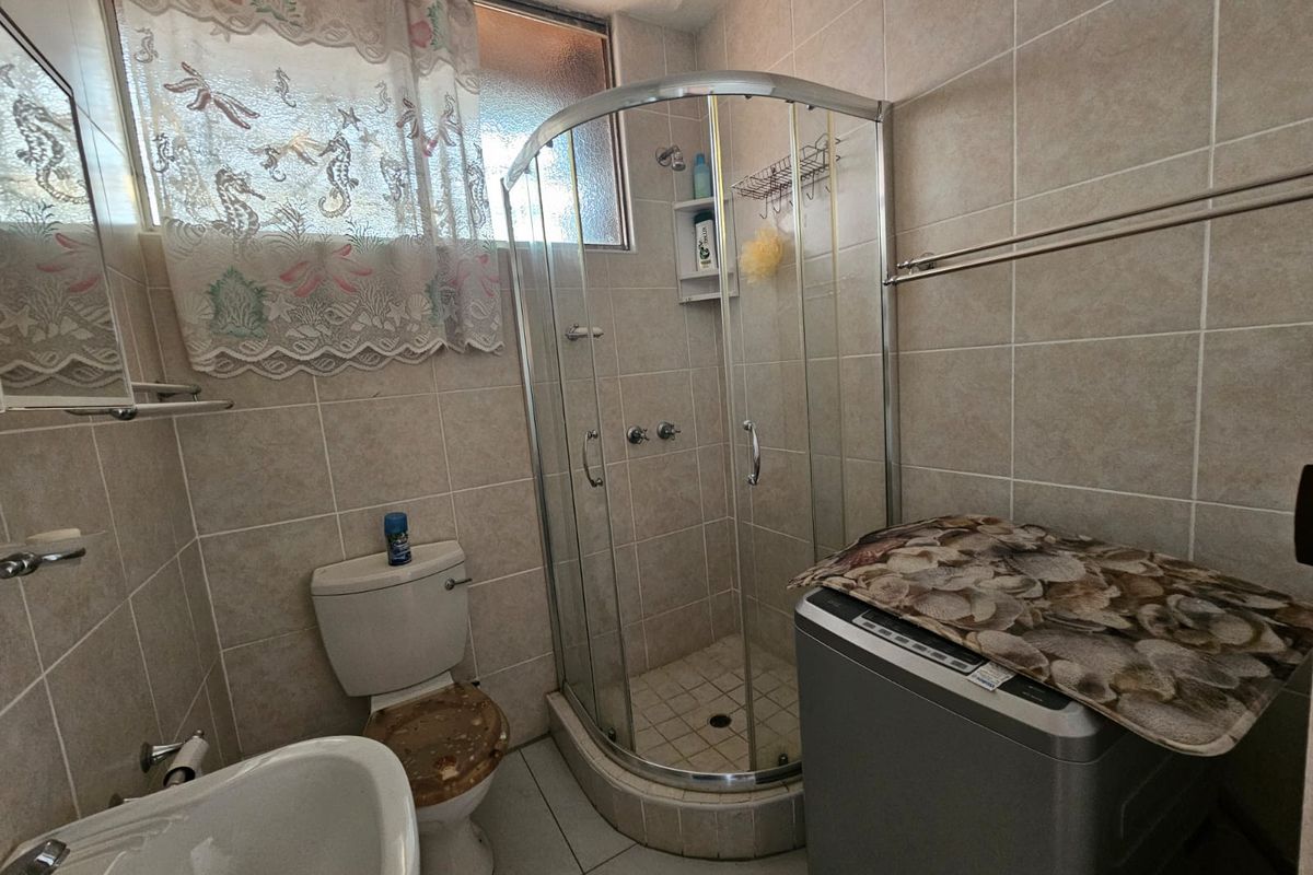 Compact bathroom featuring a corner shower enclosure, pedestal basin, and toilet with fully tiled walls and flooring.