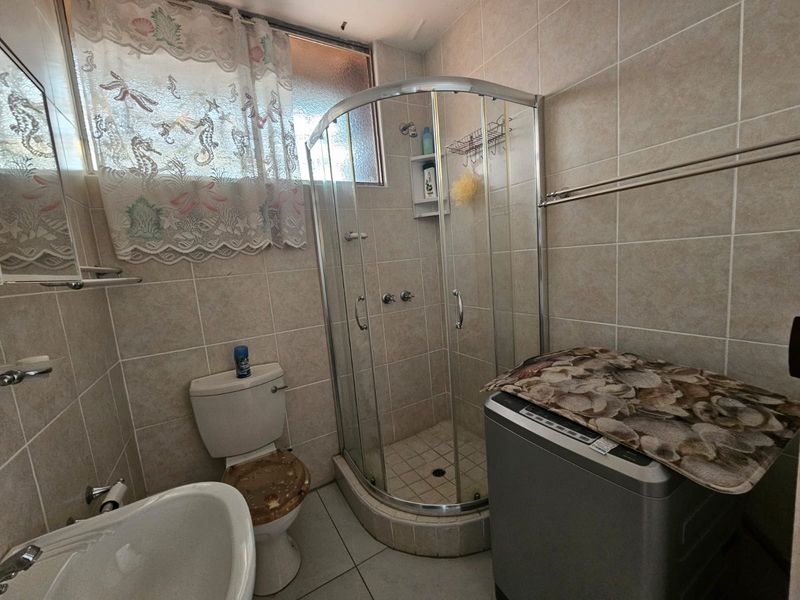 Compact bathroom featuring a corner shower enclosure, pedestal basin, and toilet with fully tiled walls and flooring.