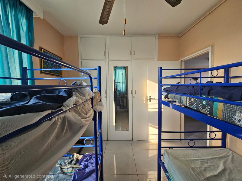 A functional bedroom featuring tiled flooring, a ceiling fan, and ample built-in cupboard storage with a central mirrored panel.