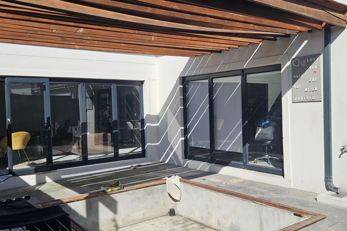 Covered patio area featuring a timber pergola, modern aluminium sliding doors, and a built-in concrete planter box, offering a functional outdoor entertainment space.