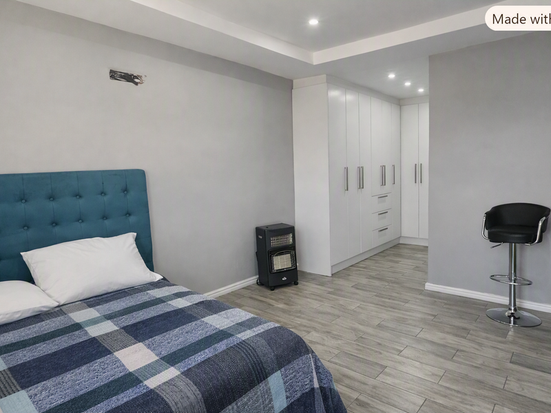 A modern bedroom featuring neutral grey walls, light wood-look tiled flooring, and extensive white built-in cabinetry with integrated recessed ceiling lighting.