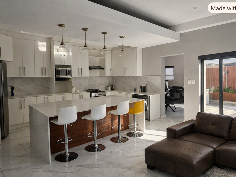 Modern open-plan kitchen featuring a large island with stone countertops, sleek white cabinetry, marble-look flooring, and seamless access to the outdoor patio area.