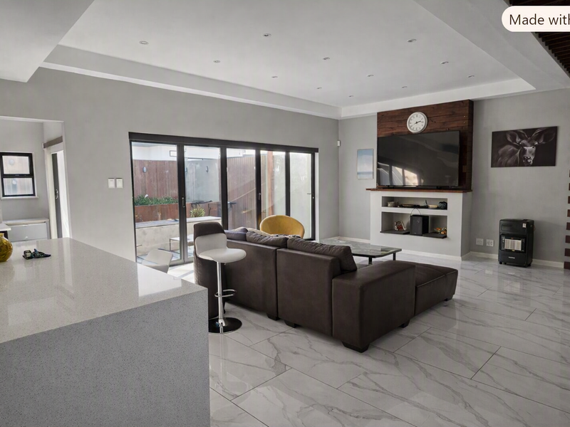 Modern open-plan living area featuring high-gloss marble-look flooring, recessed ceiling lighting, and a built-in media wall with seamless access to the outdoor patio.