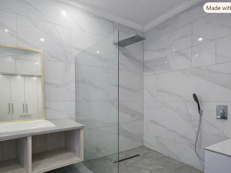 Modern bathroom featuring a walk-in shower with glass screen, rain shower head, vanity unit with integrated sink, and elegant marble-look wall tiling.